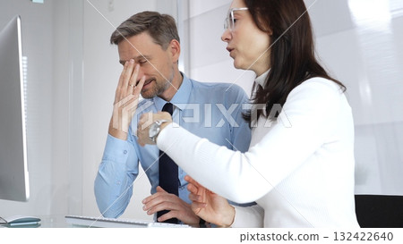 Business colleagues collaborating at office desk, discussing project on computer, man explaining screen content to woman during a corporate meeting, providing advice and support 132422640
