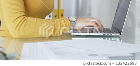 Woman working on laptop, typing on keyboard in office, managing business documents on desk, focusing on digital marketing communication and online data entry 132422698