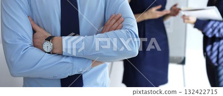 Confident businessman standing with arms crossed at a corporate meeting, leading a team of professionals discussing business strategies and plans in an office workspace 132422715