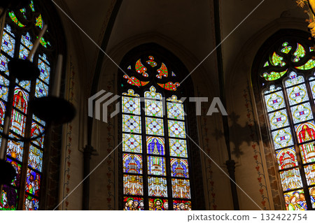 Intricate stained glass windows illuminate a historic church interior with vibrant color and sacred detail. Gothic arches symbolic imagery create a serene and spiritual atmosphere filled with light Intricate stained glass windows illuminate a historic church interior with vibrant color and sacred detail. Gothic arches symbolic imagery create a serene and spiritual atmosphere filled with light 132422754