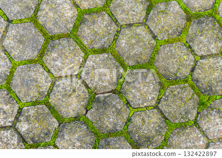 Old hexagonal stone pavement with green moss growing between cracks, creating natural geometric texture. Concept of nature reclaiming, urban decay beauty, natural vintage background Old hexagonal stone pavement with green moss growing between cracks, creating natural geometric texture. Concept of nature reclaiming, urban decay beauty, natural vintage background 132422897