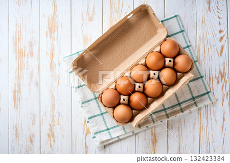 chicken eggs in a carton box on a light kitchen table, selective focus, top view. chicken eggs in a carton box on a light kitchen table, selective focus, top view. 132423384