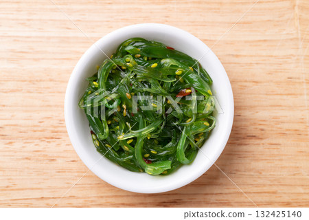 Wakame seaweed salad with sesame seed in a bowl on wooden background, Table top view Wakame seaweed salad with sesame seed in a bowl on wooden background, Table top view 132425140