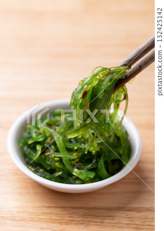 Wakame seaweed salad with sesame seed in a bowl with chopsticks on wooden background Wakame seaweed salad with sesame seed in a bowl with chopsticks on wooden background 132425142