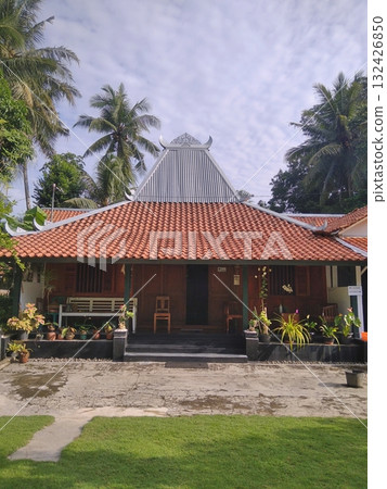 Traditional Javanese Joglo House with Terracotta Roof and Palm Trees 132426850