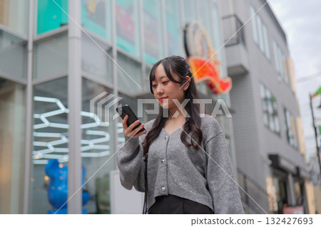 一名年輕女子一邊走在原宿的小巷裡，一邊看著她的智慧型手機 132427693