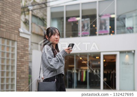 一名年輕女子一邊走在原宿的小巷裡，一邊看著她的智慧型手機 132427695