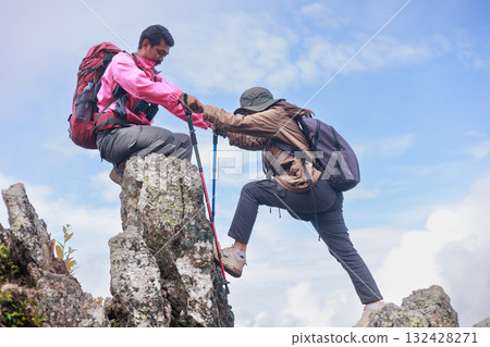 Two hikers on rocky mountain peak helping each other climb, symbol of teamwork, leadership, support, adventure, success, trust, exploration and outdoor lifestyle motivation in nature. 132428271
