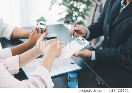 Businessman explaining car loan agreement with calculator, customer discussing auto finance deal at office desk with toy car and document, concept of vehicle loan, insurance or car leasing. car loan. 132428461