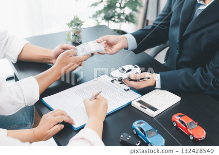 Customer paying cash to dealer with car loan contract, vehicle models on desk, concept of auto purchase, finance, leasing, insurance, successful transaction and business agreement. car loan contract Customer paying cash to dealer with car loan contract, vehicle models on desk, concept of auto purchase, finance, leasing, insurance, successful transaction and business agreement. car loan contract 132428540