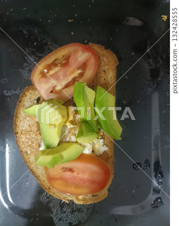 Avocado and tomato toast with egg on toasted whole grain bread, fresh breakfast with vibrant green avocado and red tomato slices 132428555