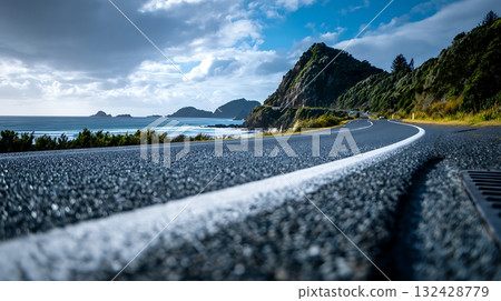Scenic Coastal Road with Lush Greenery and Distant Islands Under Cloudy Skies 132428779
