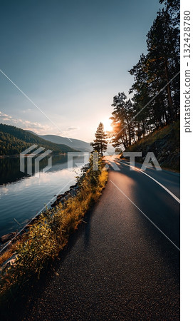 Scenic Lakeside Road at Sunset with Mountains and Trees along the Water's Edge 132428780