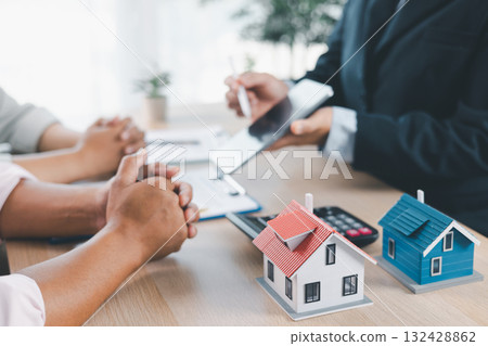 House model on desk with blurred people discussing contract in background, concept of real estate investment, mortgage loan, home ownership, property business and financial agreement. House model on desk with blurred people discussing contract in background, concept of real estate investment, mortgage loan, home ownership, property business and financial agreement. 132428862