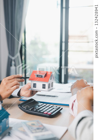 Close up of real estate agent showing small house model to client with calculator, contract paperwork on desk, concept of mortgage loan, home ownership, property investment agreement. mortgage loan Close up of real estate agent showing small house model to client with calculator, contract paperwork on desk, concept of mortgage loan, home ownership, property investment agreement. mortgage loan 132428941
