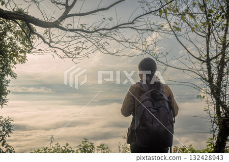 Traveler with backpack standing on mountain top looking at scenic sunrise over sea of mist, adventure lifestyle concept, hiking, freedom, exploration and outdoor travel inspiration. Traveler with backpack standing on mountain top looking at scenic sunrise over sea of mist, adventure lifestyle concept, hiking, freedom, exploration and outdoor travel inspiration. 132428943
