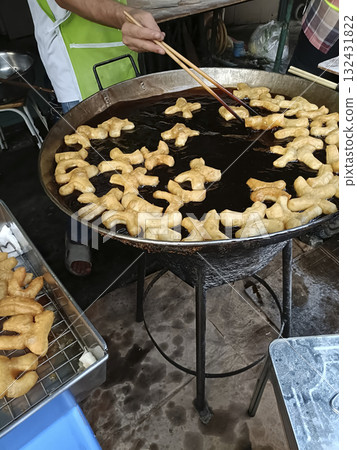 Street food vendor frying golden dough twists in large wok, hot oil, crispy texture, handmade, savory aroma, morning market Street food vendor frying golden dough twists in large wok, hot oil, crispy texture, handmade, savory aroma, morning market 132431822