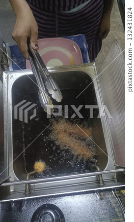 Street food fryer hot oil deep frying tongs hand night crispy snack with lively vibe Street food fryer hot oil deep frying tongs hand night crispy snack with lively vibe 132431824