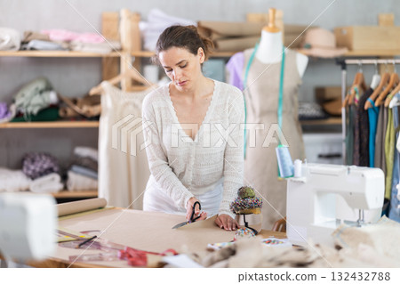 Female tailor cutting paper with scissors, cutting out the outline of pattern for a dress 132432788