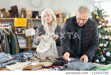 Elderly married couple choose sweater for the winter season together in fashionable clothing store. 132432789