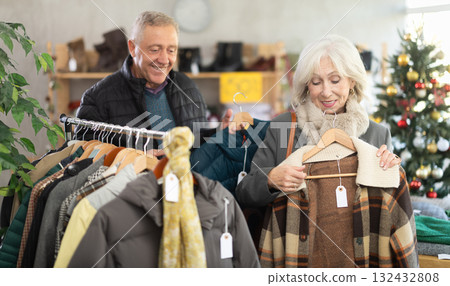 Positive mature man and woman choosing coat or jacket in clothing store Positive mature man and woman choosing coat or jacket in clothing store 132432808