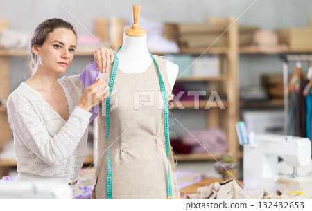 Woman tailor connects parts of dress on mannequin 132432853