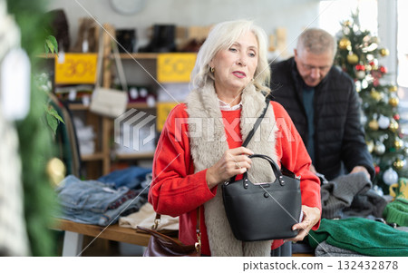 Mature woman standing and choosing handbag on Christmas tree background Mature woman standing and choosing handbag on Christmas tree background 132432878