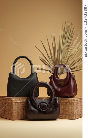 Elegant leather handbag trio neutral tones with textured wicker display and dried palm leaf for stylish still life composition, warm mood Elegant leather handbag trio neutral tones with textured wicker display and dried palm leaf for stylish still life composition, warm mood 132432897