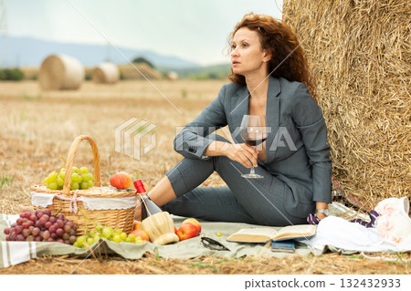 Businesswoman in revealing suit enjoying wine and reading by hay bale Businesswoman in revealing suit enjoying wine and reading by hay bale 132432933