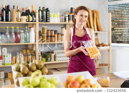 Portrait of positive female salesperson behind supermarket counter. Interior of grocery supermarket Portrait of positive female salesperson behind supermarket counter. Interior of grocery supermarket 132433056