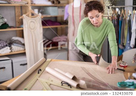 Female clothing designer cutting pattern paper in tailoring studio 132433070