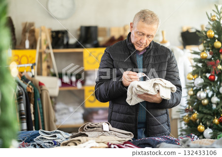 Attentive mature man choosing sweater in clothing store Attentive mature man choosing sweater in clothing store 132433106