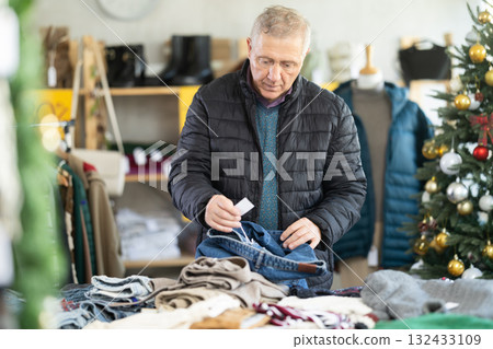 Mature man choosing jeans against the background of a Christmas tree Mature man choosing jeans against the background of a Christmas tree 132433109