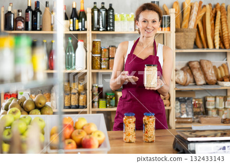 Friendly female seller offers to buy canned beans in interior of grocery supermarket 132433143