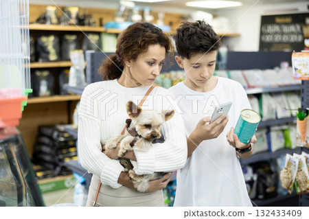Teenager with mother scanning label on dog food can with smartphone in pet store 132433409
