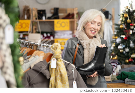 Mature woman standing on the background of a Christmas tree and choosing platform boots 132433458