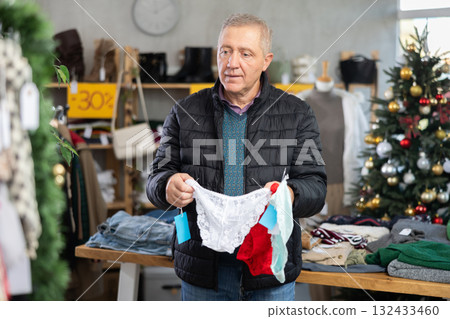 Mature male shopper selects ladies panties as a Christmas gift in fashionable clothing boutique Mature male shopper selects ladies panties as a Christmas gift in fashionable clothing boutique 132433460