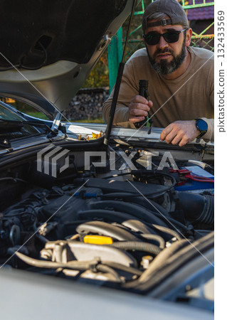 Man inspecting car engine with flashlight in outdoor setting Man inspecting car engine with flashlight in outdoor setting 132433569