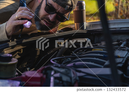 Man inspects car engine with flashlight in outdoor area 132433572