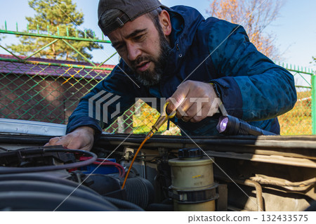 Man inspecting car engine during sunny day in a rural area 132433575