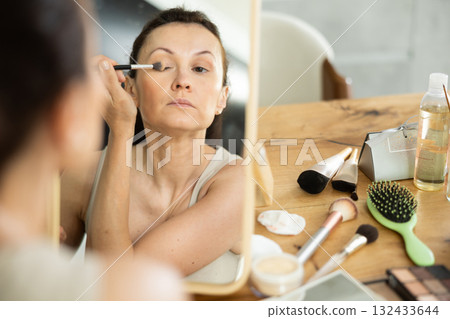 Woman applying eyeshadow with brush during daily makeup 132433644