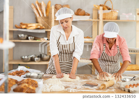 Two female bakers kneading dough and shaping pieces Two female bakers kneading dough and shaping pieces 132433650
