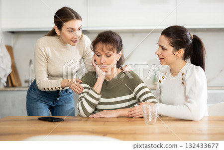 Sad middle-aged woman sitting at table while two others trying to calm her 132433677