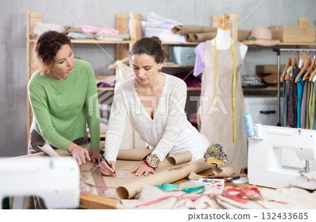 Two female dress designers developing new patterns on paper in studio 132433685