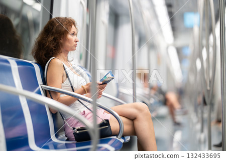 Adult woman sitting in subway car with phone Adult woman sitting in subway car with phone 132433695