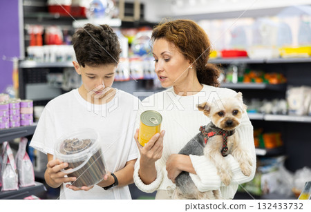 Mother with dog Yorkshire Terrier in arms and son carefully examine label on dry dog food Mother with dog Yorkshire Terrier in arms and son carefully examine label on dry dog food 132433732