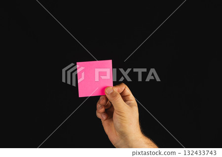 Hand holding a pink sticky note against a black background 132433743