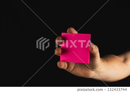 Person holding bright pink sticky note against a dark background Person holding bright pink sticky note against a dark background 132433744