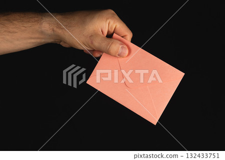 Hand holding a pink envelope in front of a dark background during evening Hand holding a pink envelope in front of a dark background during evening 132433751