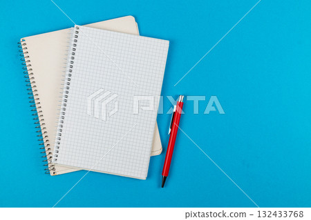 Red pen and blank notebooks on a bright blue backdrop 132433768